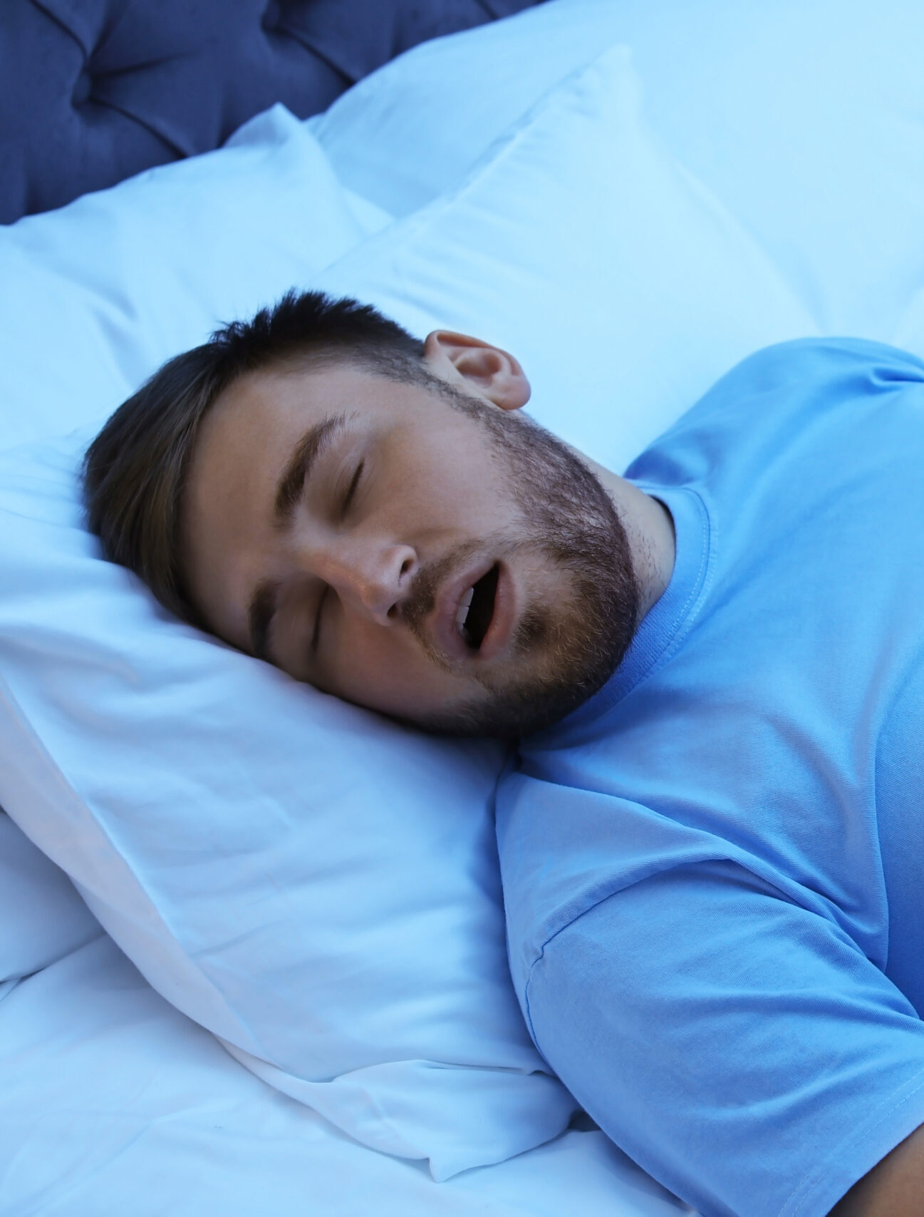 Young man snoring while sleeping in bed at night. Sleep disorder