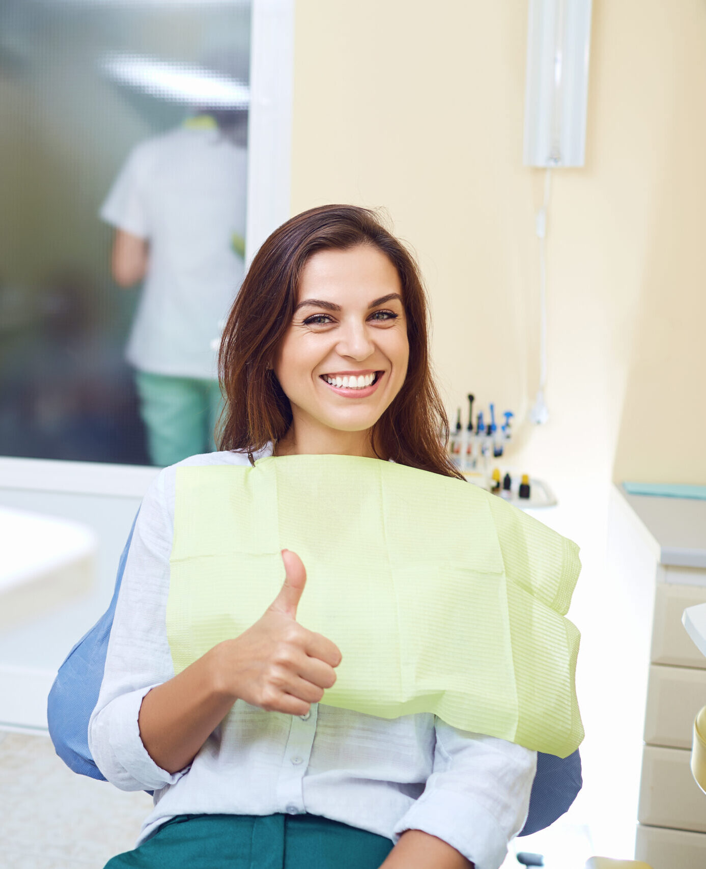 Patient woman smiling holding thumbs up at the dental clinic.