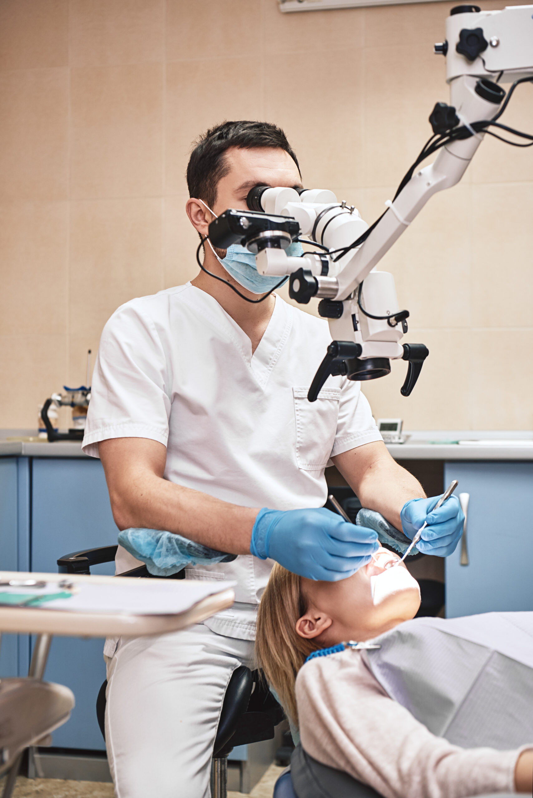 Male dentist wearing white uniform, looking into professional dental endodontic binocular microscope with camera in the office. Dental tools. Treatment. Vertical shot