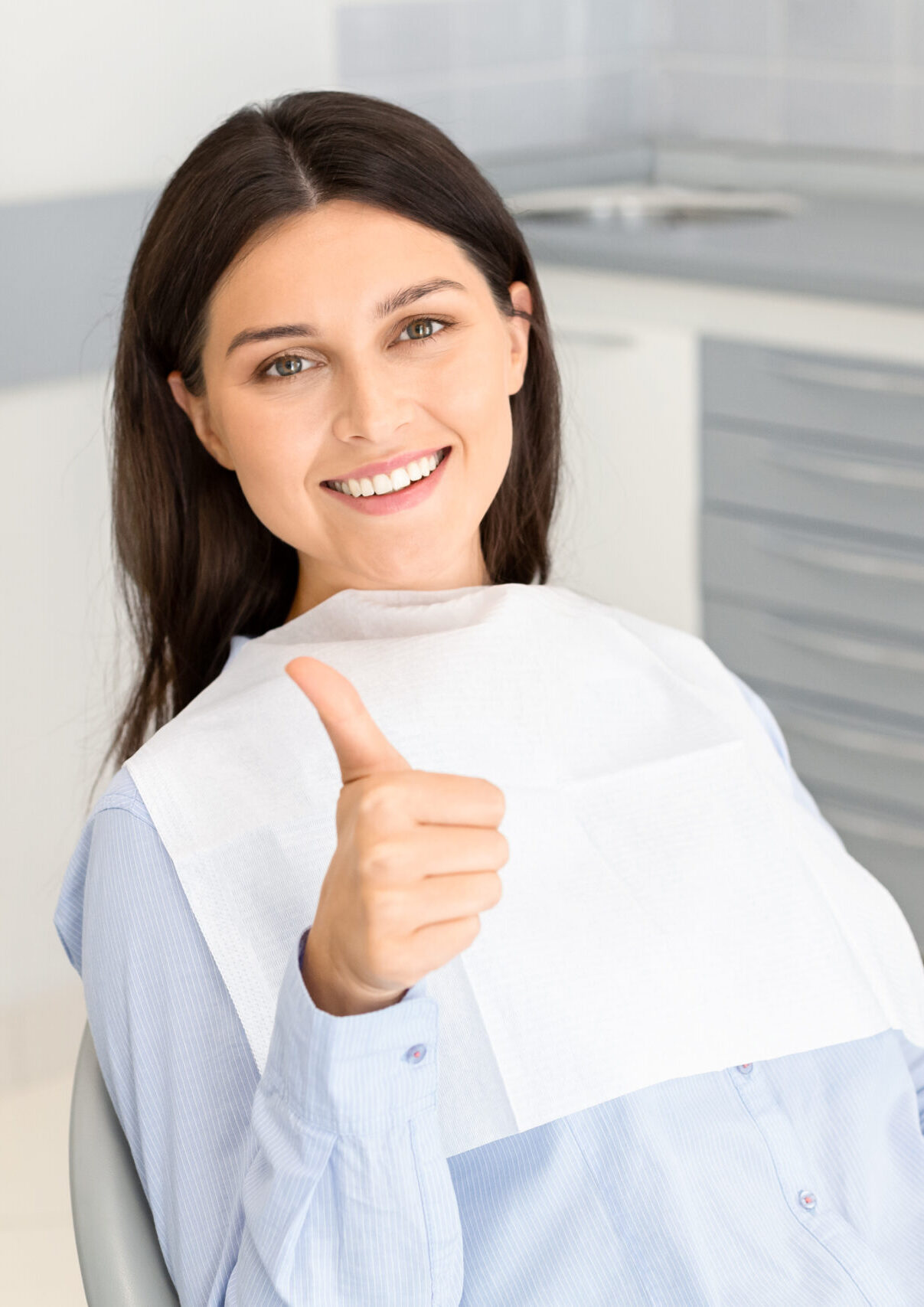 Portrait of pretty brunette female patient smiling and showing thumb up in dentistry, free space