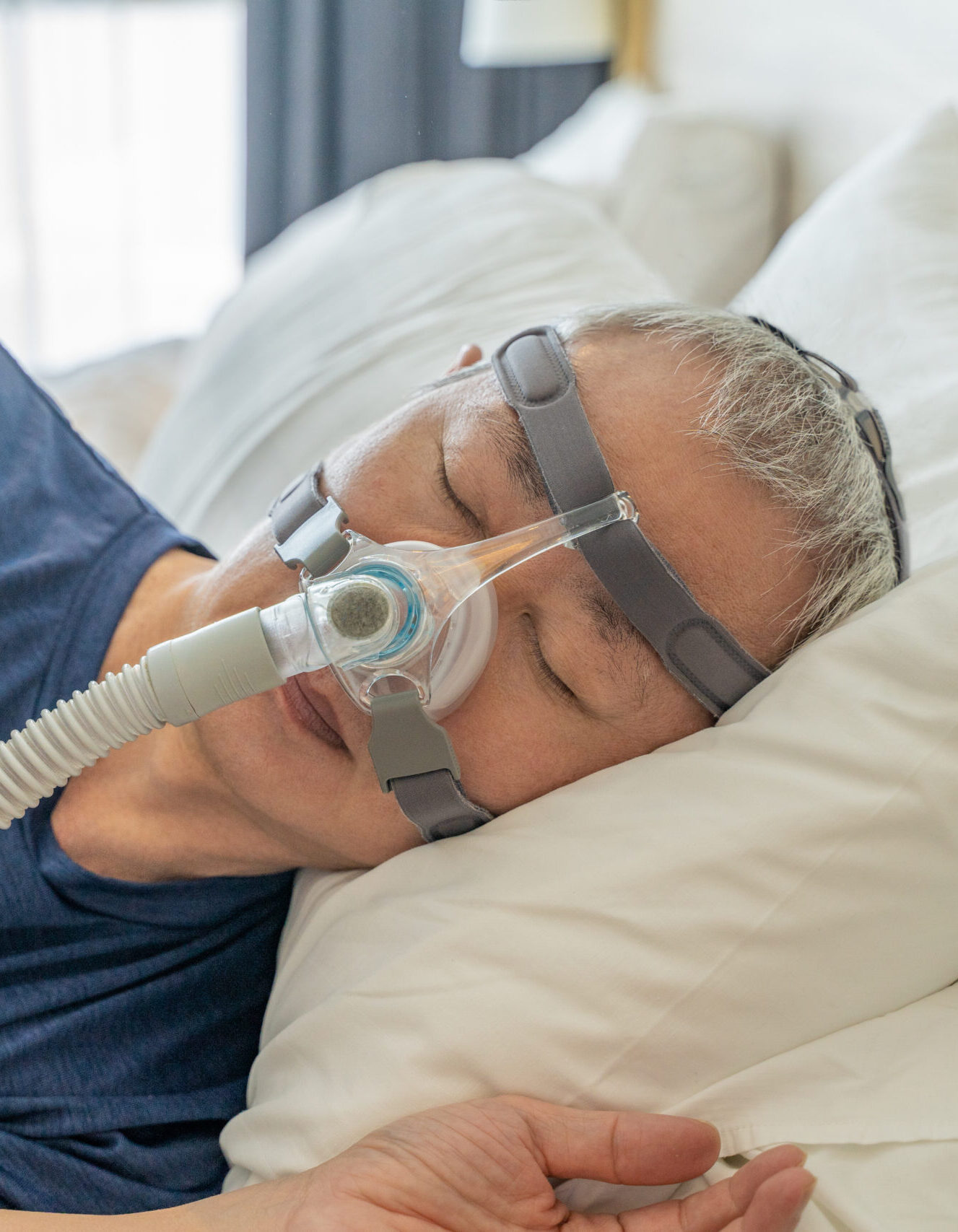 Middle age man wearing CPAP mask and headgear to help with his sleep apnea while sleeping in his bed in his bedroom