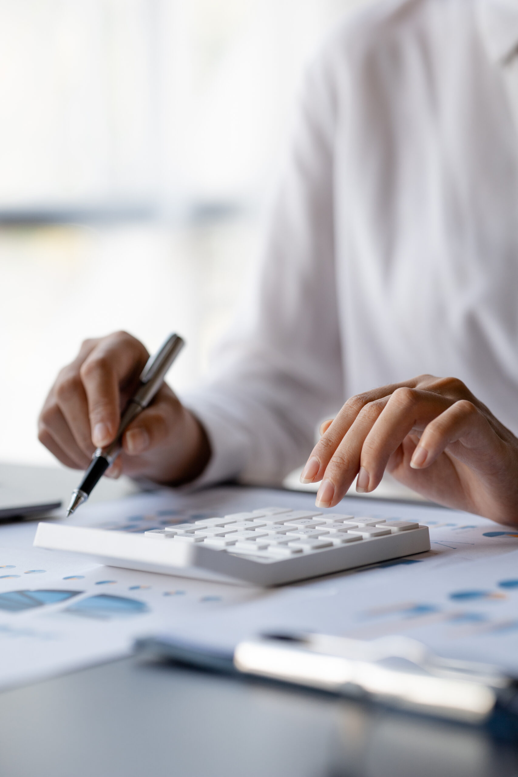 Businessman is using a calculator to calculate company financial figures from earnings papers, a businessman sitting in his office where the company financial chart is placed.