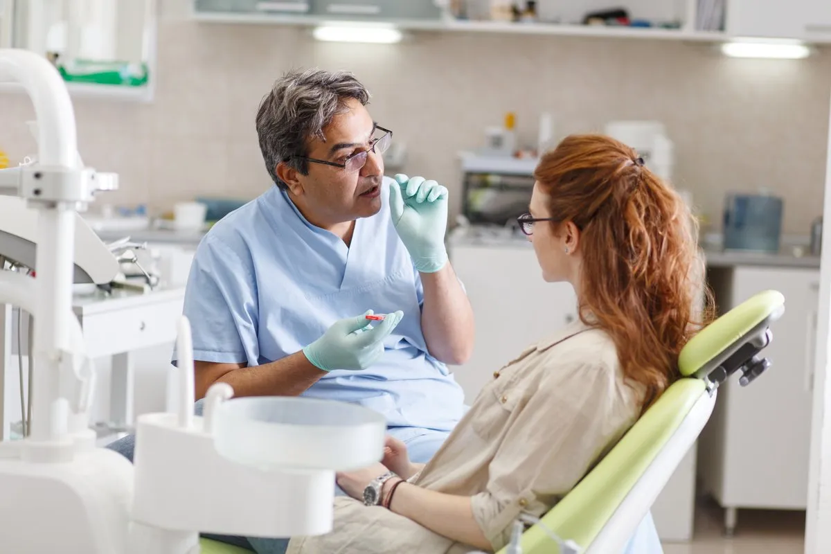 A professional dentist, equipped with a bright smile, converses with his red-haired female patient, carefully explaining the upcoming treatment, and ensuring her comfort throughout the process.