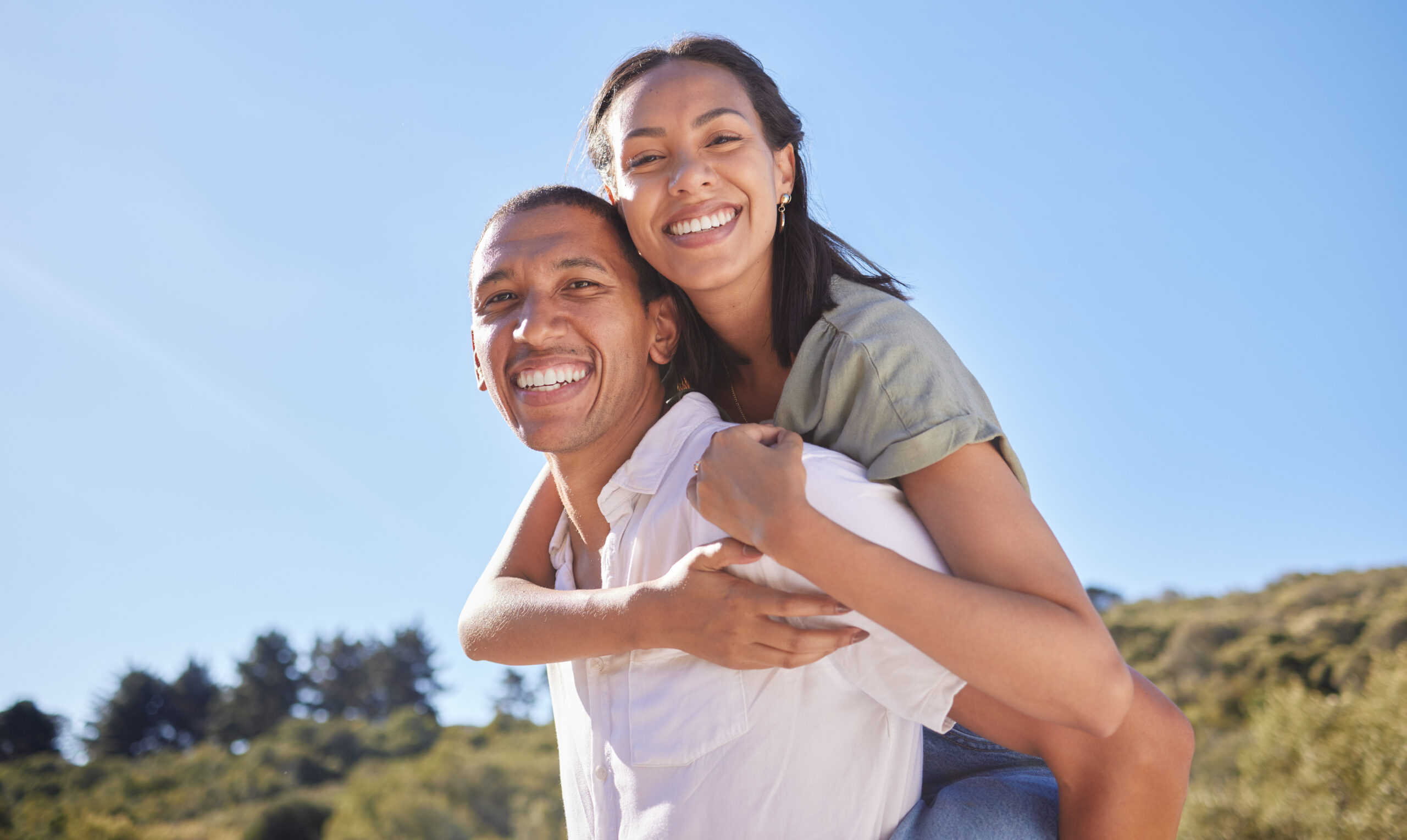 Love, happy couple and travel adventure with young lovers out hiking, exploring and traveling through nature in summer. Portrait smile of latino man and woman enjoying piggyback while out for a walk.