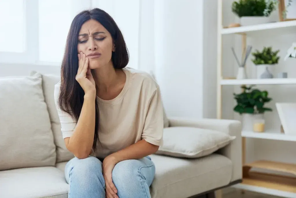 Woman toothache, tooth root inflammation sitting on sofa at home