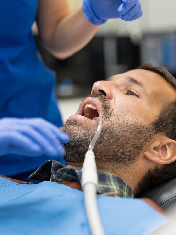A patient is seated in a dentist's chair with a focus on care and hygiene, receiving careful attention from a dental professional in a modern clinic during a procedure.