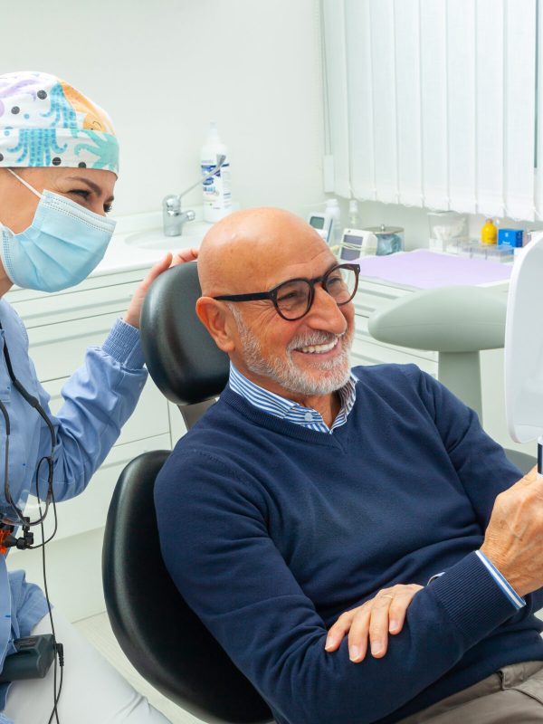 Dentist showing treatment result to happy senior patient in dental clinic