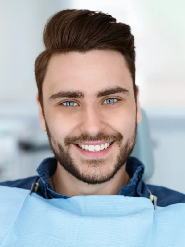 Cheerful bearde man patient sitting in dental chair and smiling at camera, copy space. Positive millennial guy showing his beautiful white smile after treatment at modern dental clinic