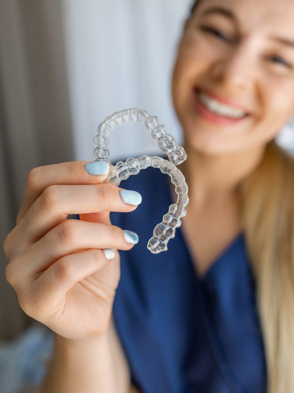 A smiling individual showcases a pair of transparent aligners, emphasizing modern orthodontic treatments for dental alignment, promoting oral health and their aesthetically pleasing