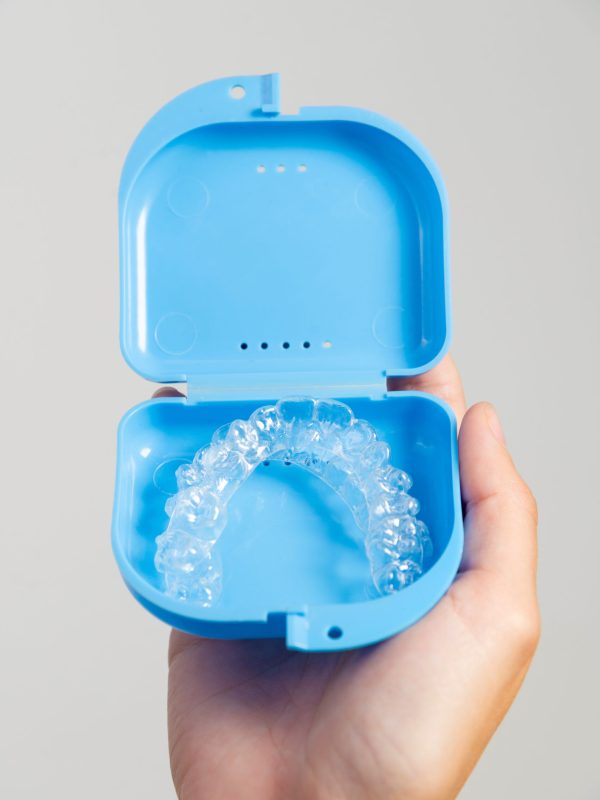 Transparent dental aligners in a case for storage and transportation are held by a woman's hand. Aesthetic and convenient correction of jaw bite. Copy space.