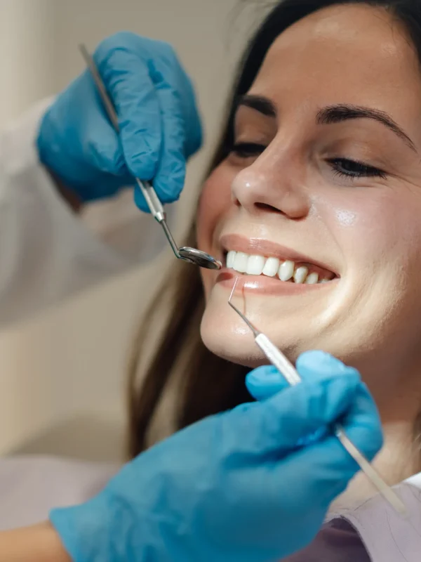 Dentist wearing blue gloves examining teeth of smiling young woman during a thorough dental checkup in a bright, clean clinic, ensuring optimal oral health and hygiene