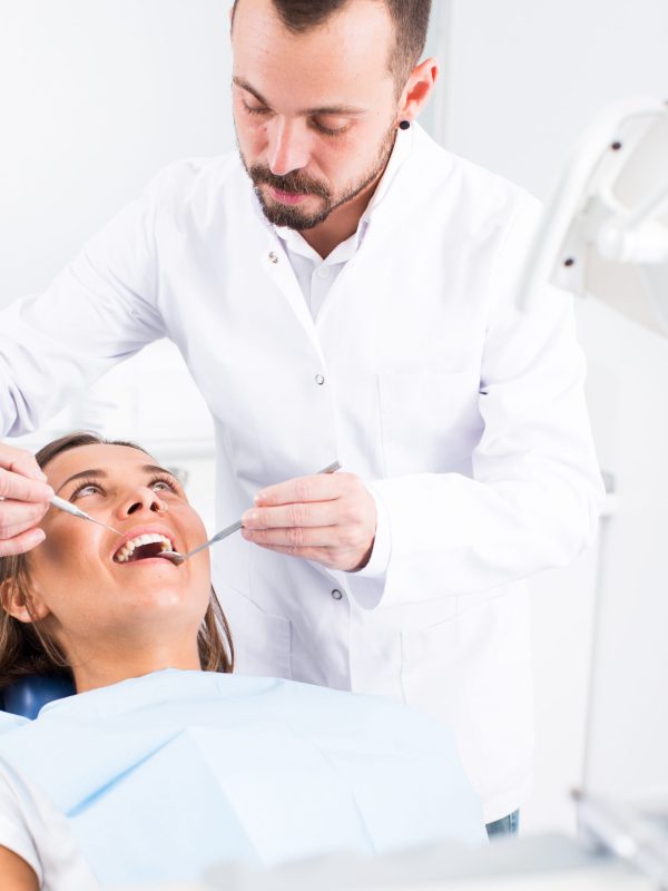 Dentist is treating woman patient which is sitting in dental chair in clinic
