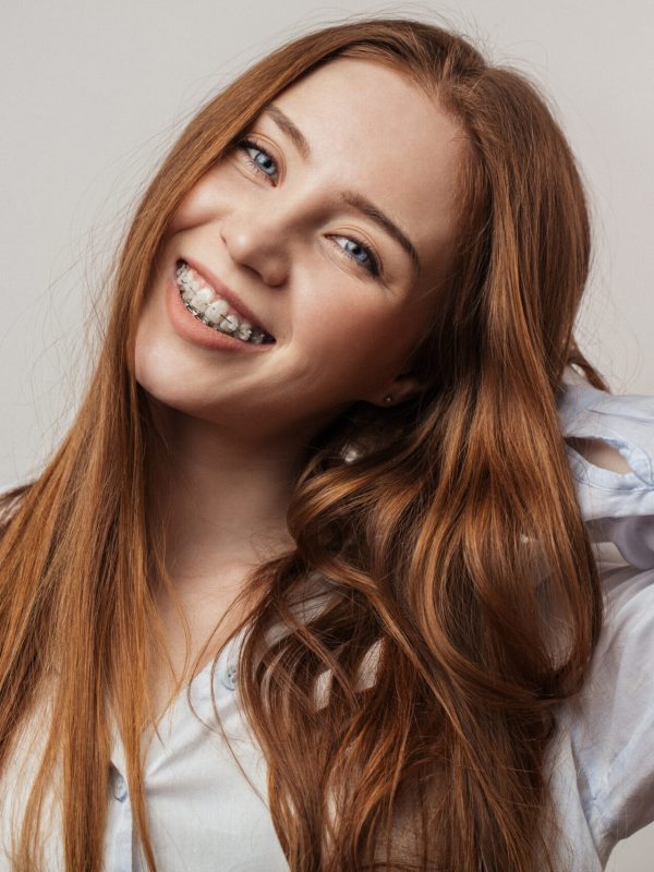 Happy young red-haired woman in braces smiling on white background looking at camera