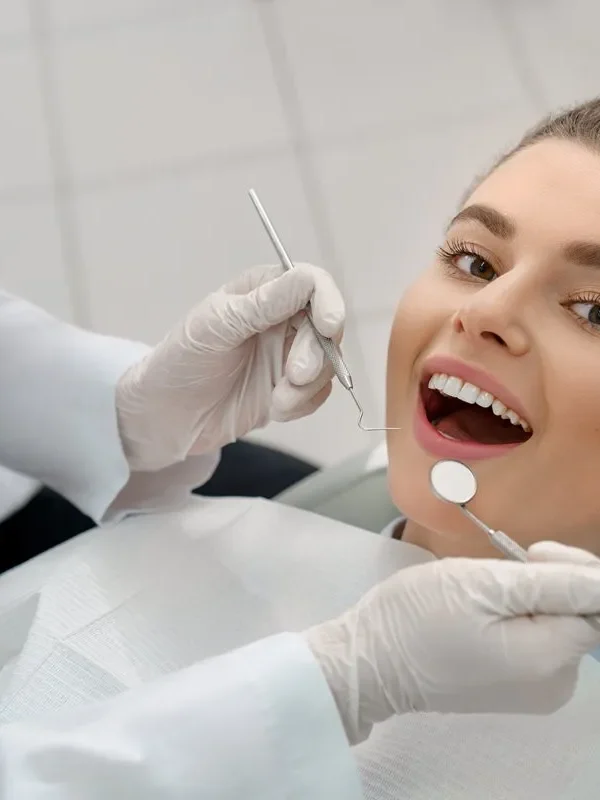 View from above of young woman lying on dental chair with open mouth and looking at camera while professional doctor checking teeth. Concept of dentistry procedure and stomatology.