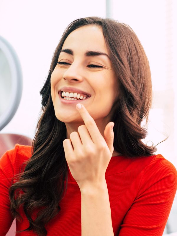 Tooth range. Hilarious girl with long curly hair in the dental chair of tooth center is using a mirror to see the result of the stomatology work which was done perfectly.