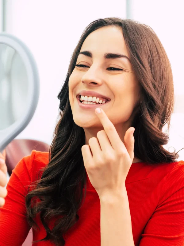Tooth range. Hilarious girl with long curly hair in the dental chair of tooth center is using a mirror to see the result of the stomatology work which was done perfectly.