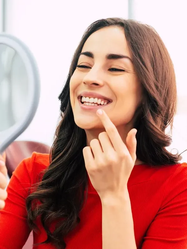 Tooth range. Hilarious girl with long curly hair in the dental chair of tooth center is using a mirror to see the result of the stomatology work which was done perfectly.