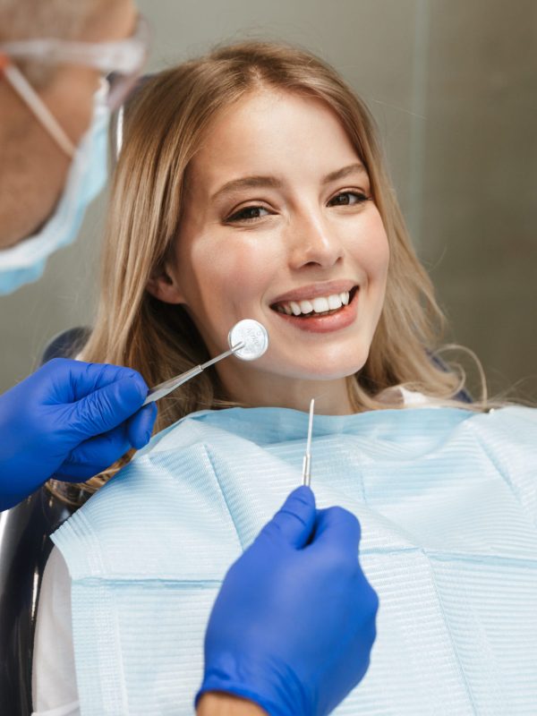 Image of content young woman sitting in dental chair at medical center while professional doctor fixing her teeth