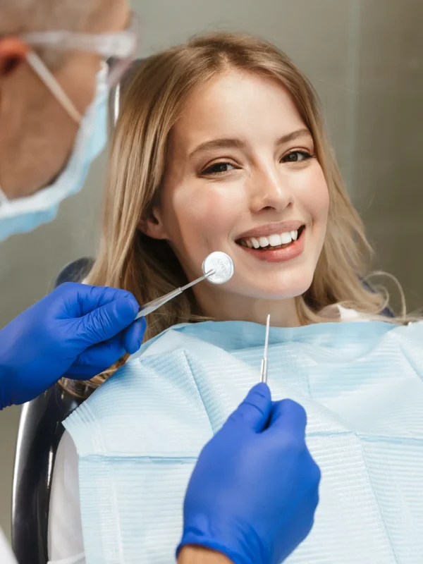 Image of content young woman sitting in dental chair at medical center while professional doctor fixing her teeth