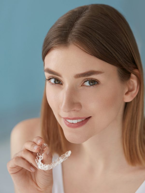 Dental care. Smiling woman with healthy teeth using removable clear braces aligner, orthodontic silicone trainer. Portrait girl with white smile using invisible whitening tray