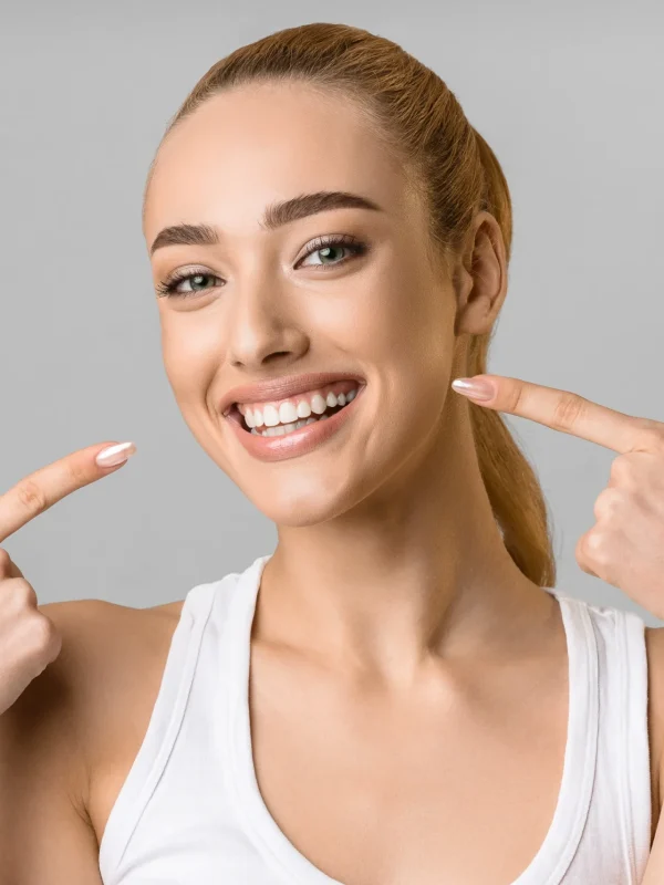 Orthodontic concept. Happy girl showing her beaming white teeth with two forefingers, grey background