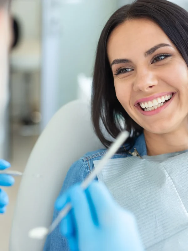smiling woman in dental chair with doctor holding dental mirror