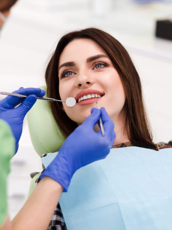 Beautiful young woman doing tooth examination in the dental office. Portrait of smiling girl on a dental chair in dentistry