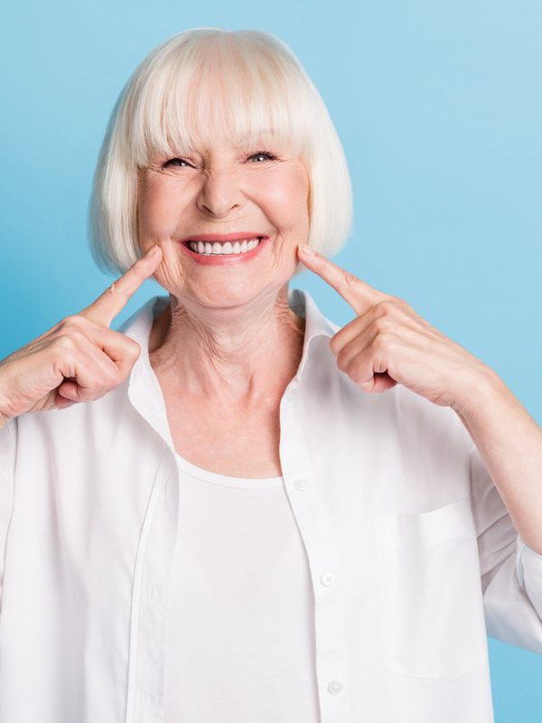 Photo portrait of granny blonde hair pointing at white teeth healthy smile dental whitening veneers isolated on bright blue color background.