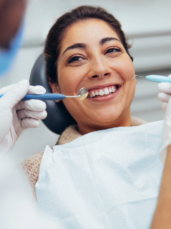 Over the shoulder view of a dental doctor treating female patient. Female having routine dental checkup at dentist.