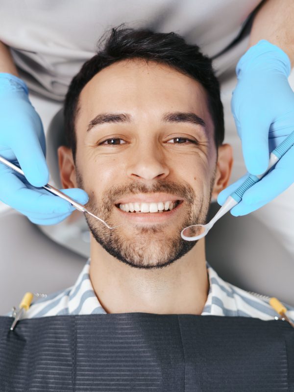 Smiling young man sitting in dentist chair while doctor examining his teeth
