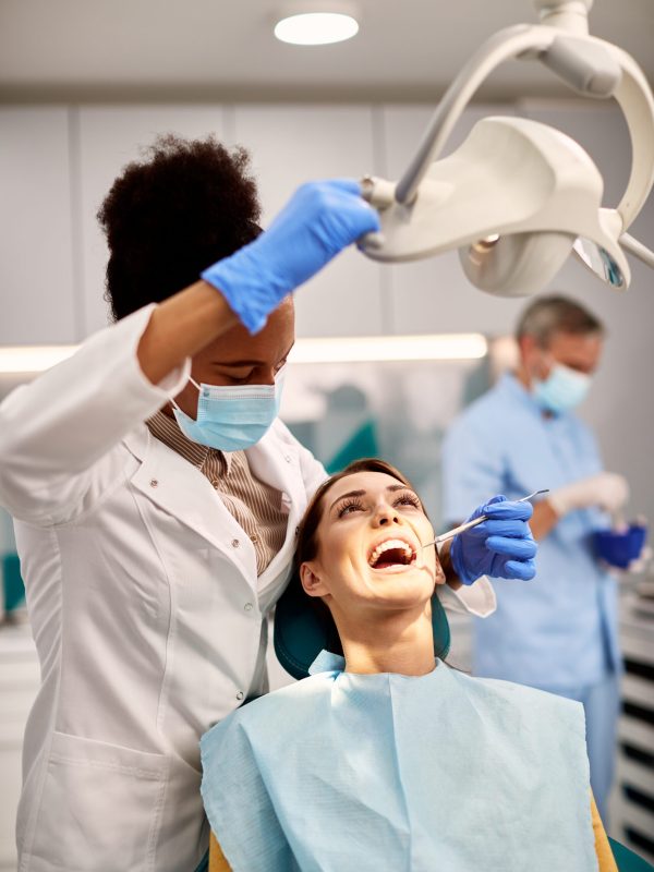 Black female dentist checking lingual dental braces of female patient during appointment at dental clinic.