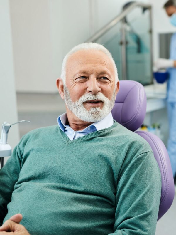 Happy senior man talks to his dentist during appointment at dental clinic.