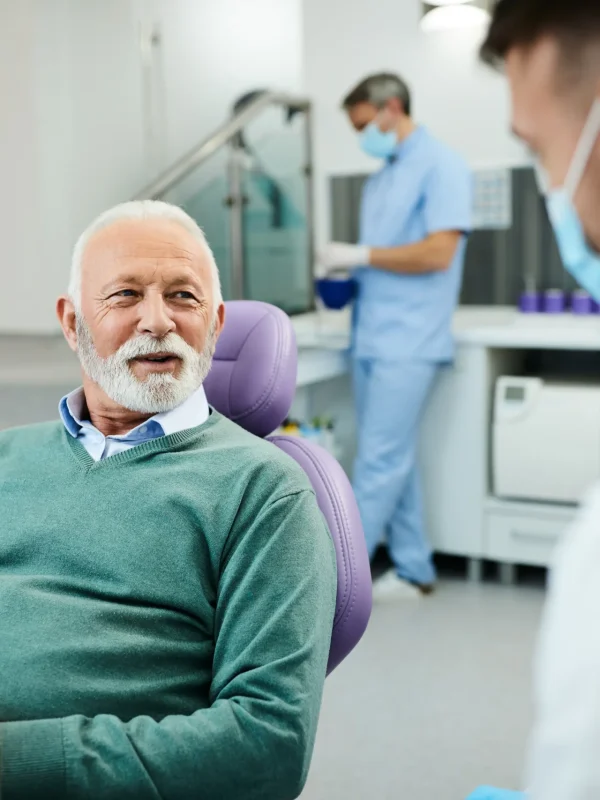 Happy senior man talks to his dentist during appointment at dental clinic.