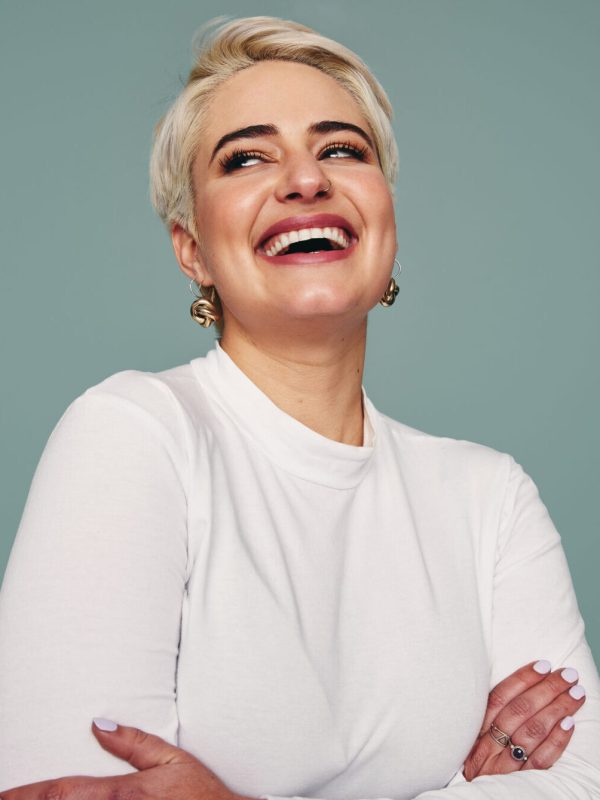 Beautiful blonde woman laughing in a studio. Happy mid-adult woman looking away cheerfully while standing against a studio background. Fashionable woman feeling confident.