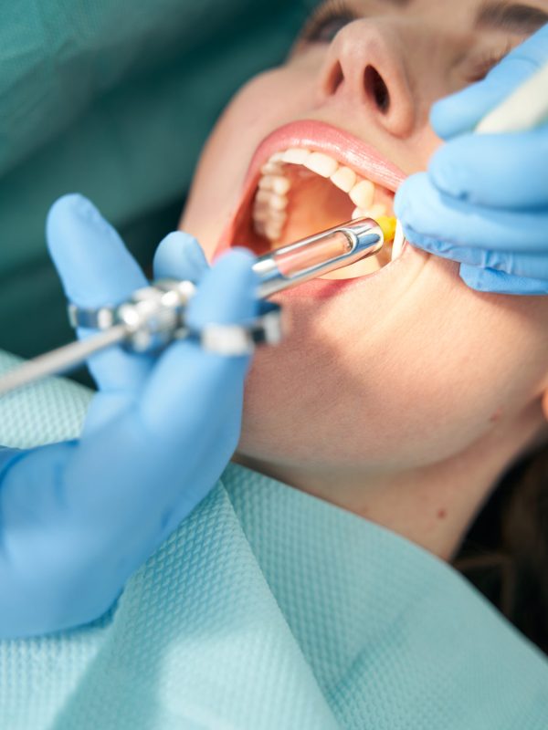 Close up of stomatologist hands in sterile gloves inserting needle into woman gum while doing local anesthesia injection before dental procedure
