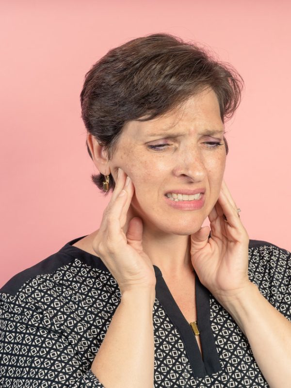 Brunette woman in her 50s in the studio with a pink background with TMJ issues