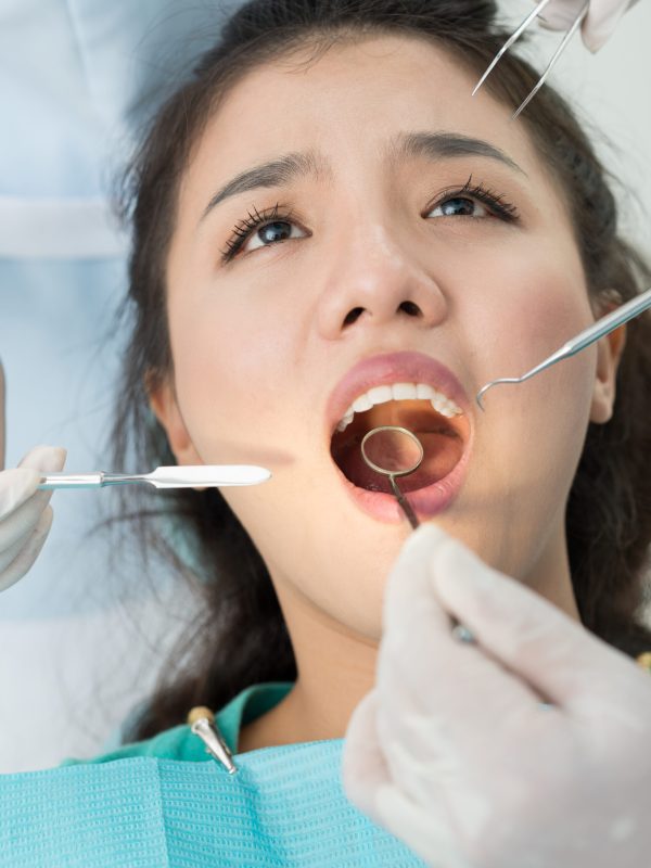 Vertical image of a patient and doctor’s hands with dental equipment in hands
