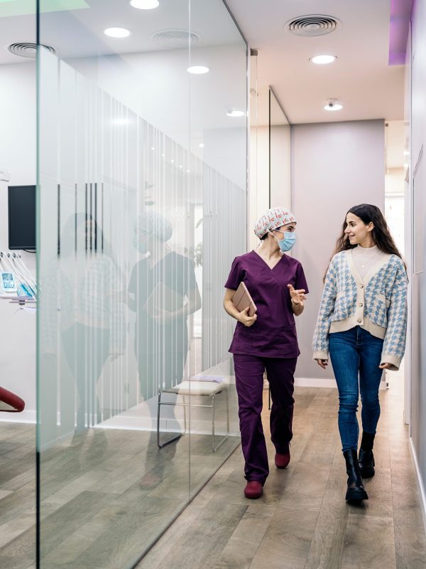 Stock photo of female dentist wearing face mask talking with her young patient in the dental clinic.