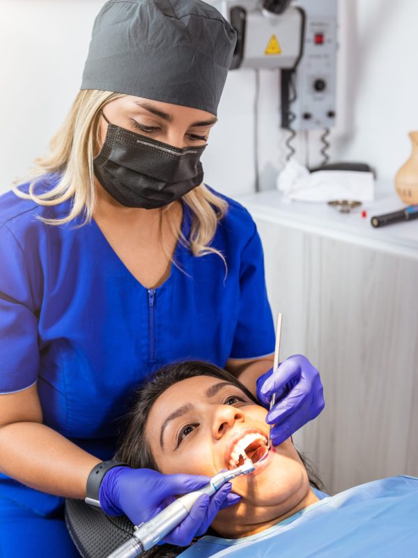 A Female odontologist attends a patient with dental instruments in her mouth during in a clinical setting