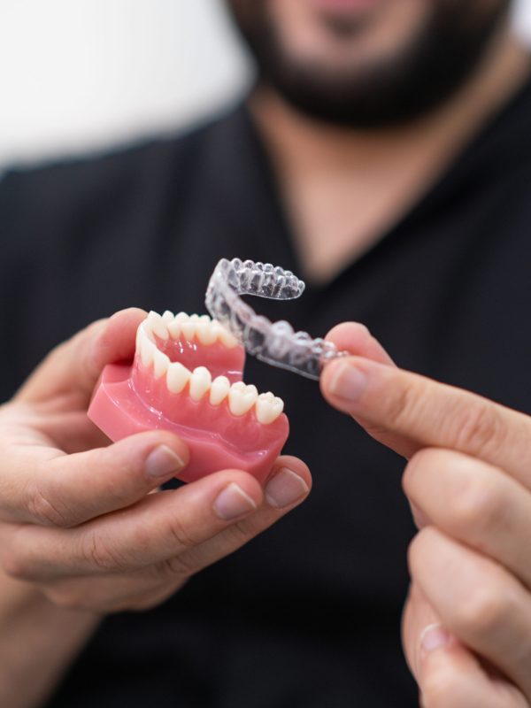 Doctor demonstrating clear aligners installation on artificial lower human jaw for orthodontic treatment in clinic dentist showing teeth maintaining tool closeup