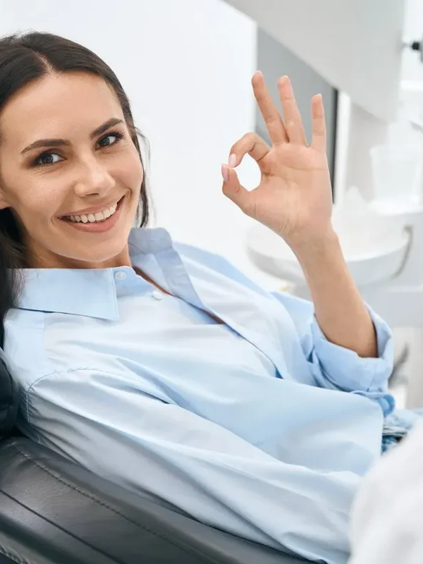 Positive woman client of stomatological clinic showing ok sign gesture sitting on orthodontic chair, enjoying good service in private dental clinic, routine teeth check-up