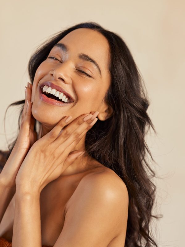 Multiethnic young woman touching her clean and healthy face against background with closed eyes. Latin hispanic woman feeling good with perfet skincare routine. Natural beauty portrait of mexican girl with black long hair.