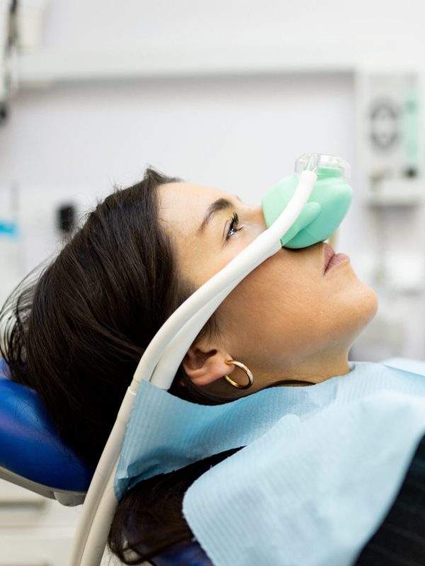 An adult woman sits in a dentist's office wearing a nasal mask to inhale nitrous oxide. Dentist fear concept. Feeling of relaxation with laughing gas. Visit a dentist with relaxation.