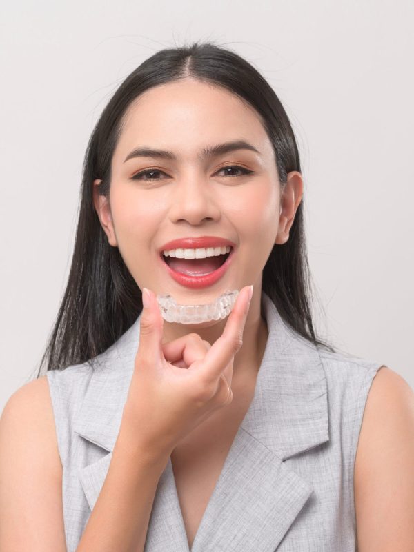 Young smiling woman holding invisalign braces in studio, dental healthcare and Orthodontic concept