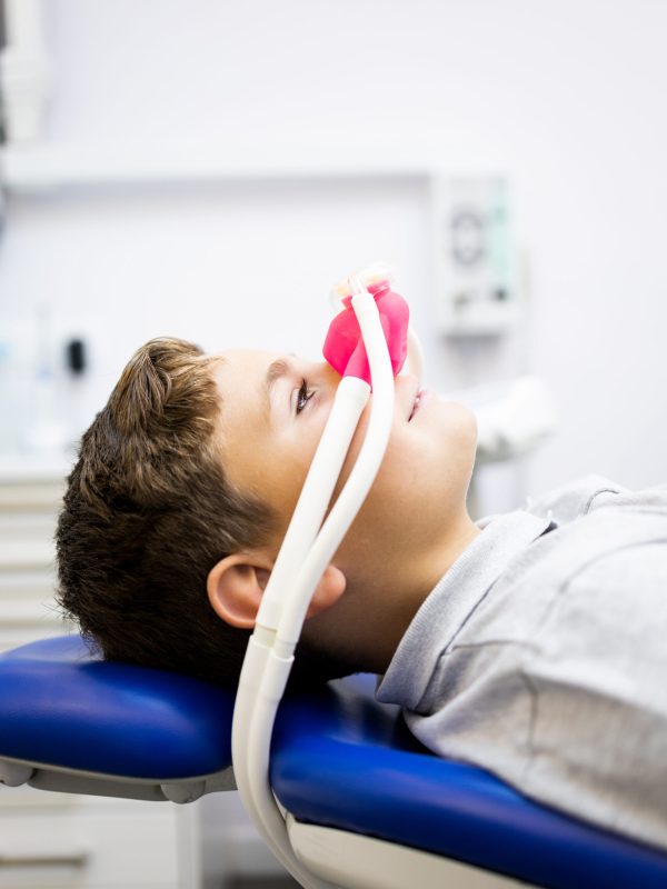 Fear of the dentist! Vertical photo of a little boy sits in a dentist's office wearing a nasal mask breathing nitrous oxide to relax. Concept of feeling relaxed with laughing gas.