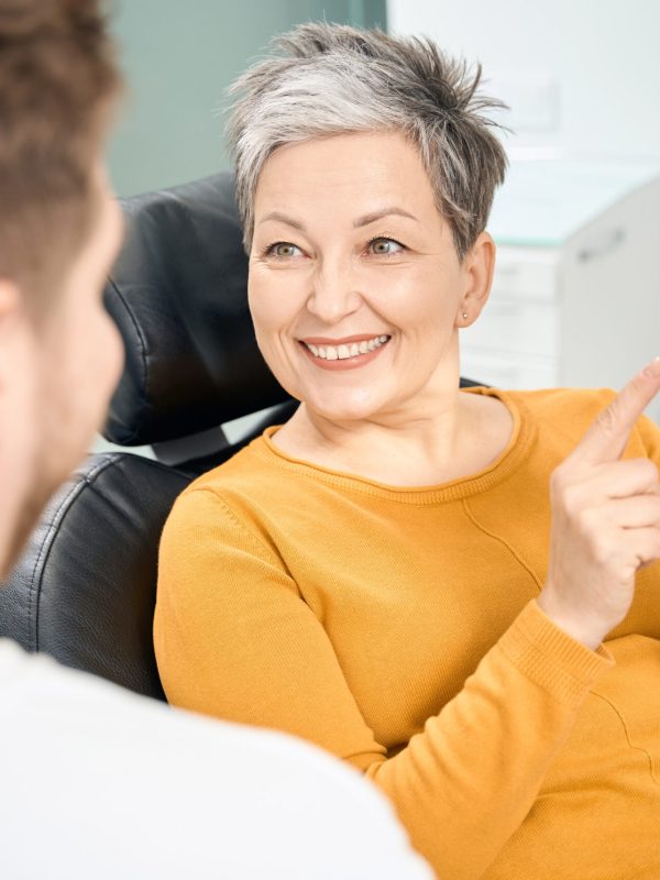 Positive adult woman client of aesthetic dentistry clinic visiting doctor office to discuss the theme of dental implants or dentures, holding in hands 3d teeth model