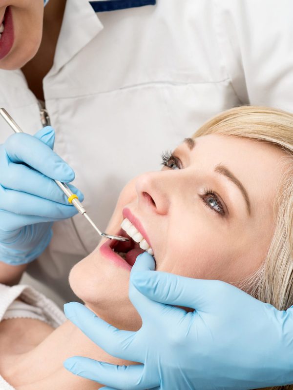 Female dentist examining teeth using mirror in clinic