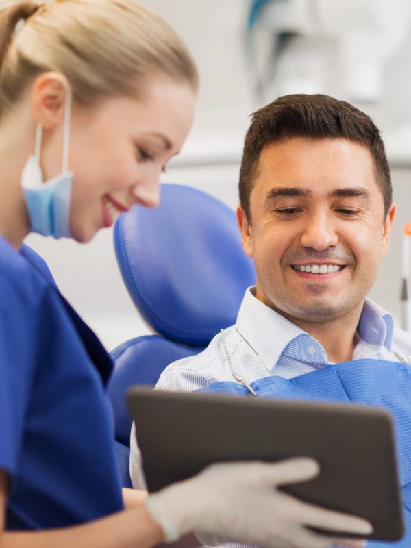 people, medicine, stomatology and health care concept - happy female dentist showing tablet pc computer to male patient at dental clinic office
