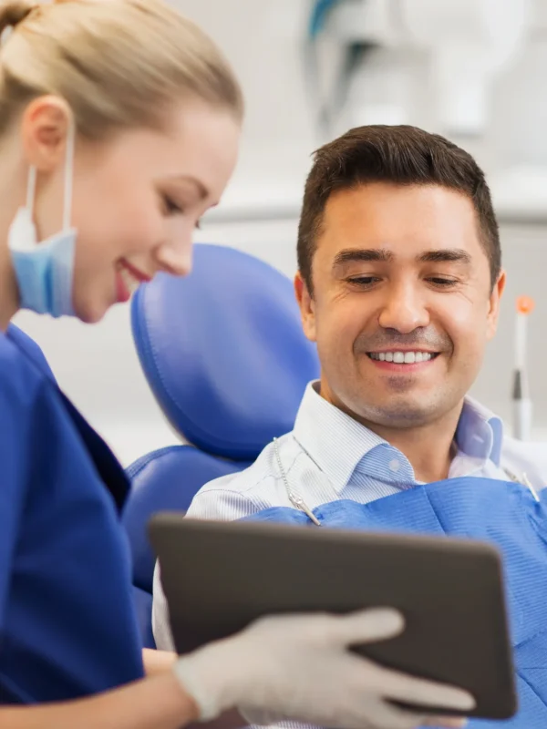 people, medicine, stomatology and health care concept - happy female dentist showing tablet pc computer to male patient at dental clinic office