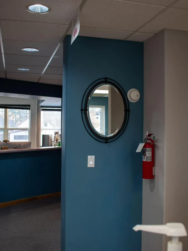 Rivers Dentistry hallway with teal accent wall, oval mirror, and reception window
